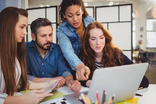 Teacher pointing at laptop with coworkers at desk in creative office Teacher pointing at laptop with coworkers at desk in creative office