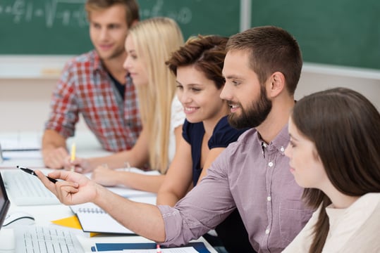 Diverse group of attractive young university students studying together sitting at a table sharing a computer monitor Diverse group of attractive young university students studying together sitting at a table sharing a computer monitor