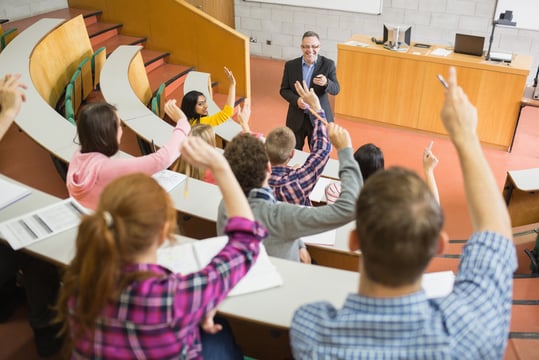 Rear view of students raising hands with a teacher in the college lecture hall Rear view of students raising hands with a teacher in the college lecture hall